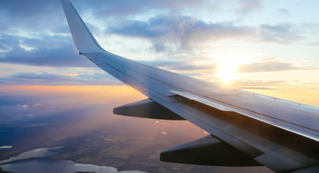 Airplane flying from Belgrade to Berlin, over Hungary, Austria, Czech Republic, Slovakia and Germany. Beautiful sunset over the airplane wing and the blue skies on the horizon over the land. People traveling.